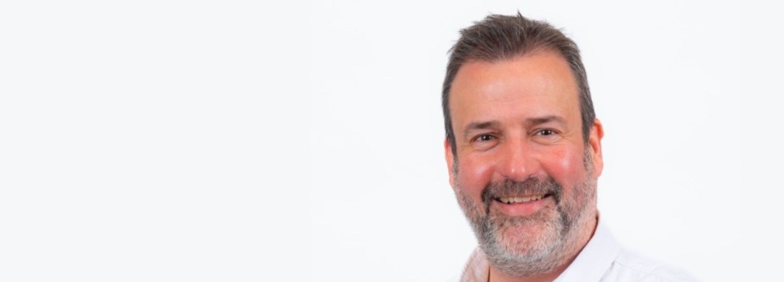 Headshot of a smiling man with short dark hair and a beard against a plain light background.